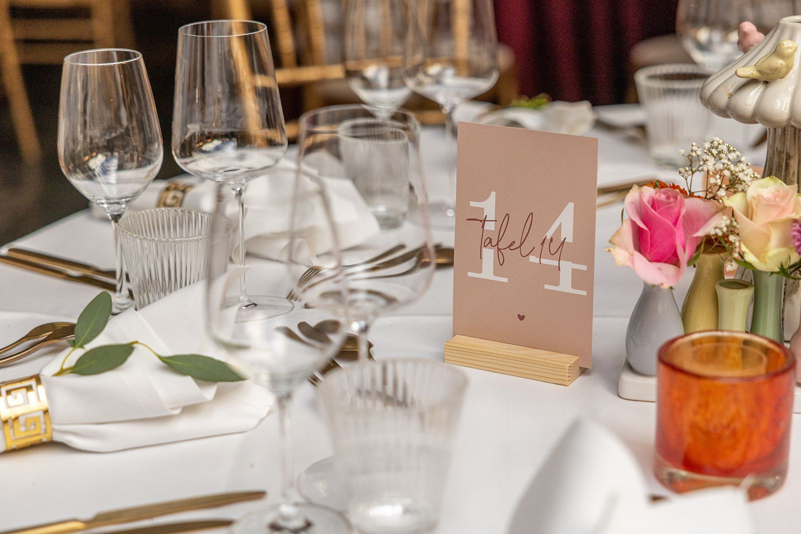 Elegante tafeldekking met tafelnummer 14, bloemen en glaswerk.
