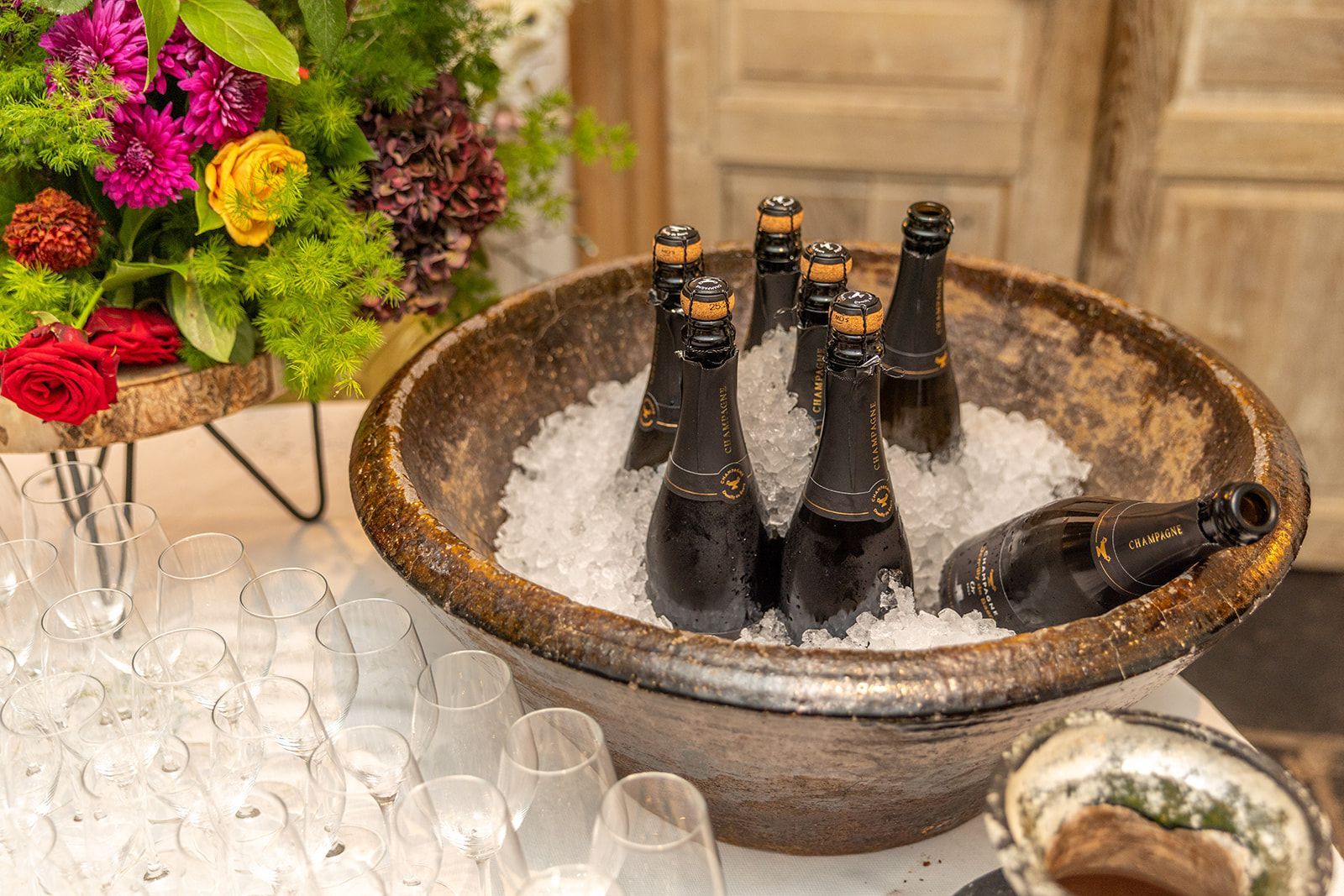 Champagneflessen in een met ijs gevulde schaal, met bloemen en champagneglazen ernaast.