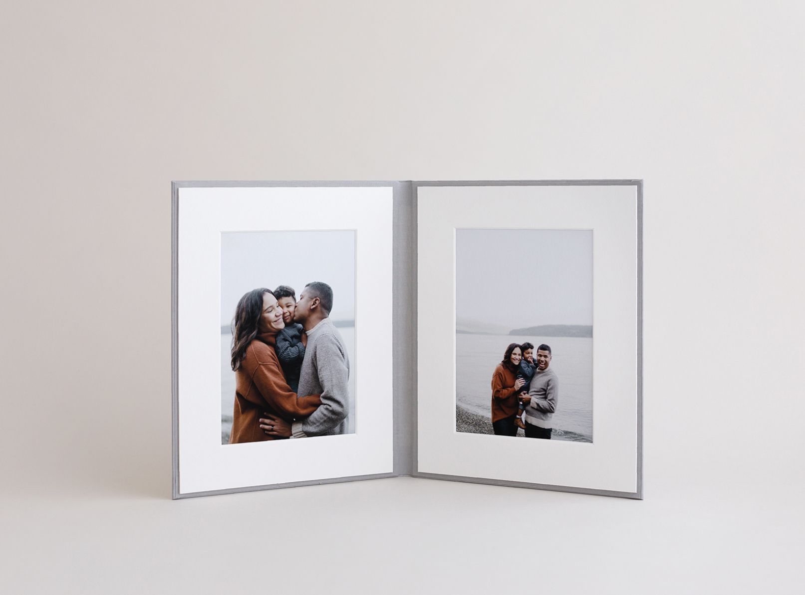 Fotolijst met twee panelen met familiefoto's: kussend stel en gezin bij het water. Zilveren lijst, witte passe-partouts.