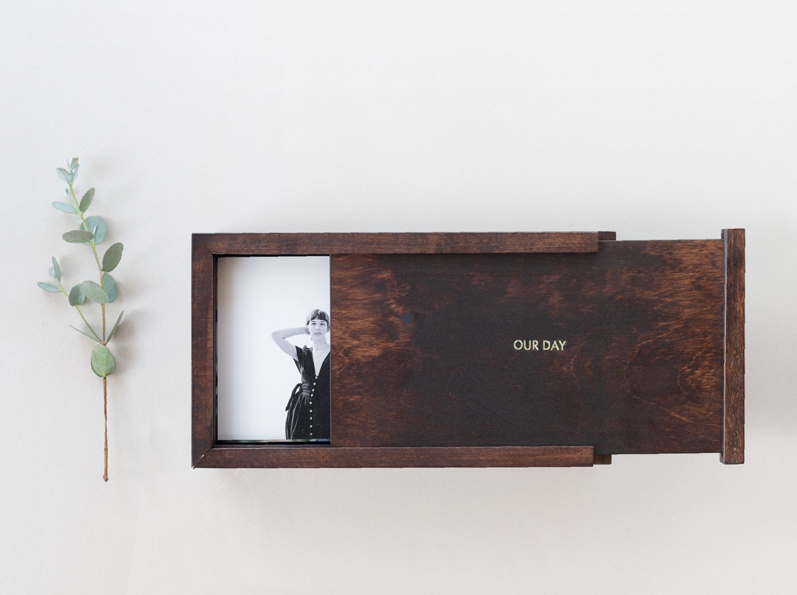 Houten fotodoos met een zwart-witafdruk, naast een takje groene bladeren.