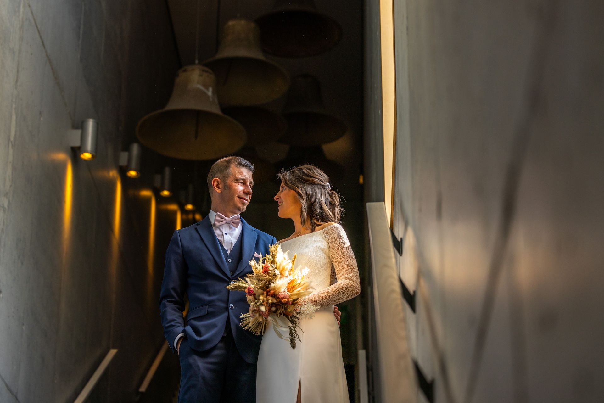Bruid en bruidegom kijken elkaar aan. Ze staan ​​op de trap, verlicht door warm licht, met klokvormige lampen erboven.