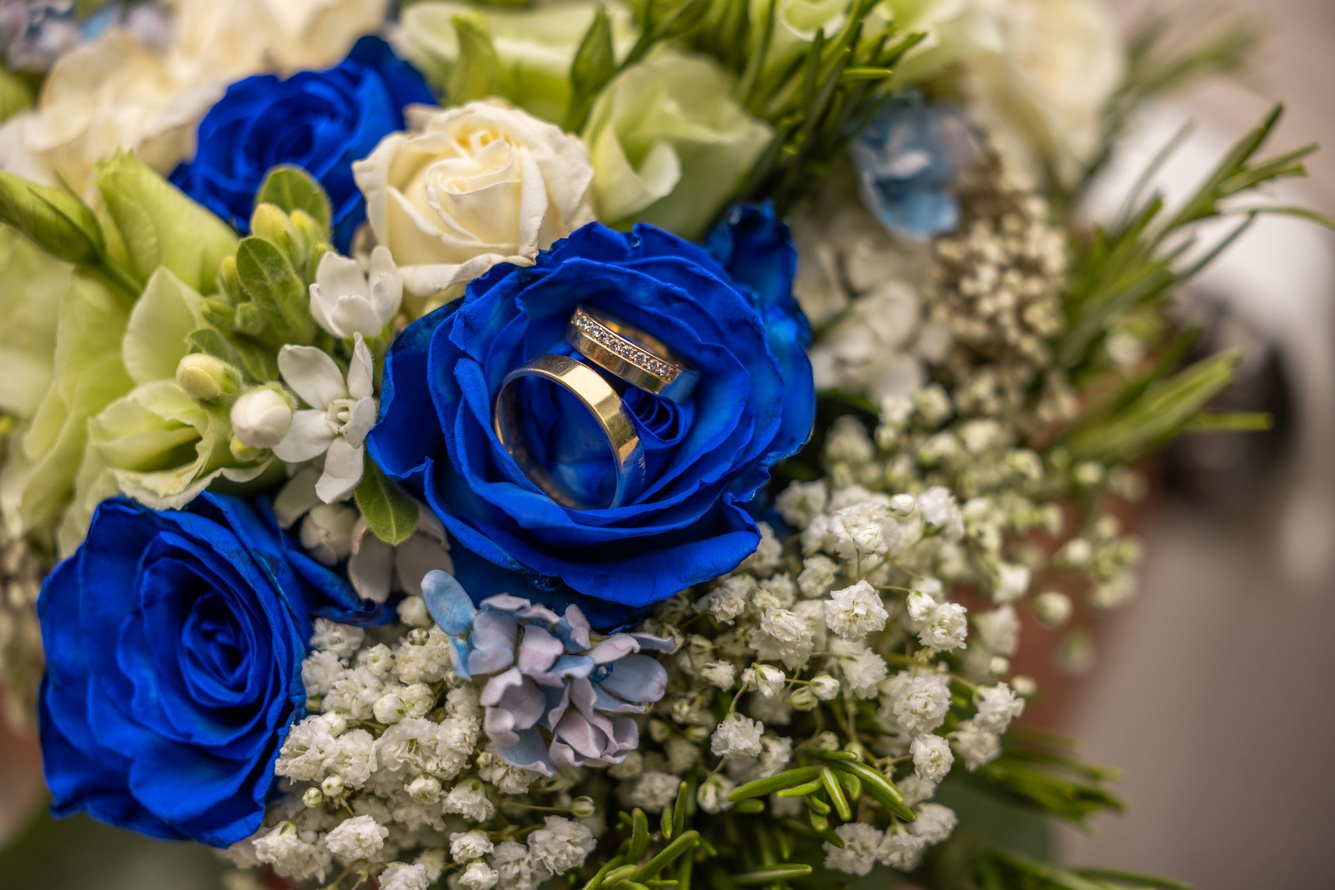 Trouwringen in levendige blauwe rozen in een boeket van witte, crèmekleurige en groene bloemen.