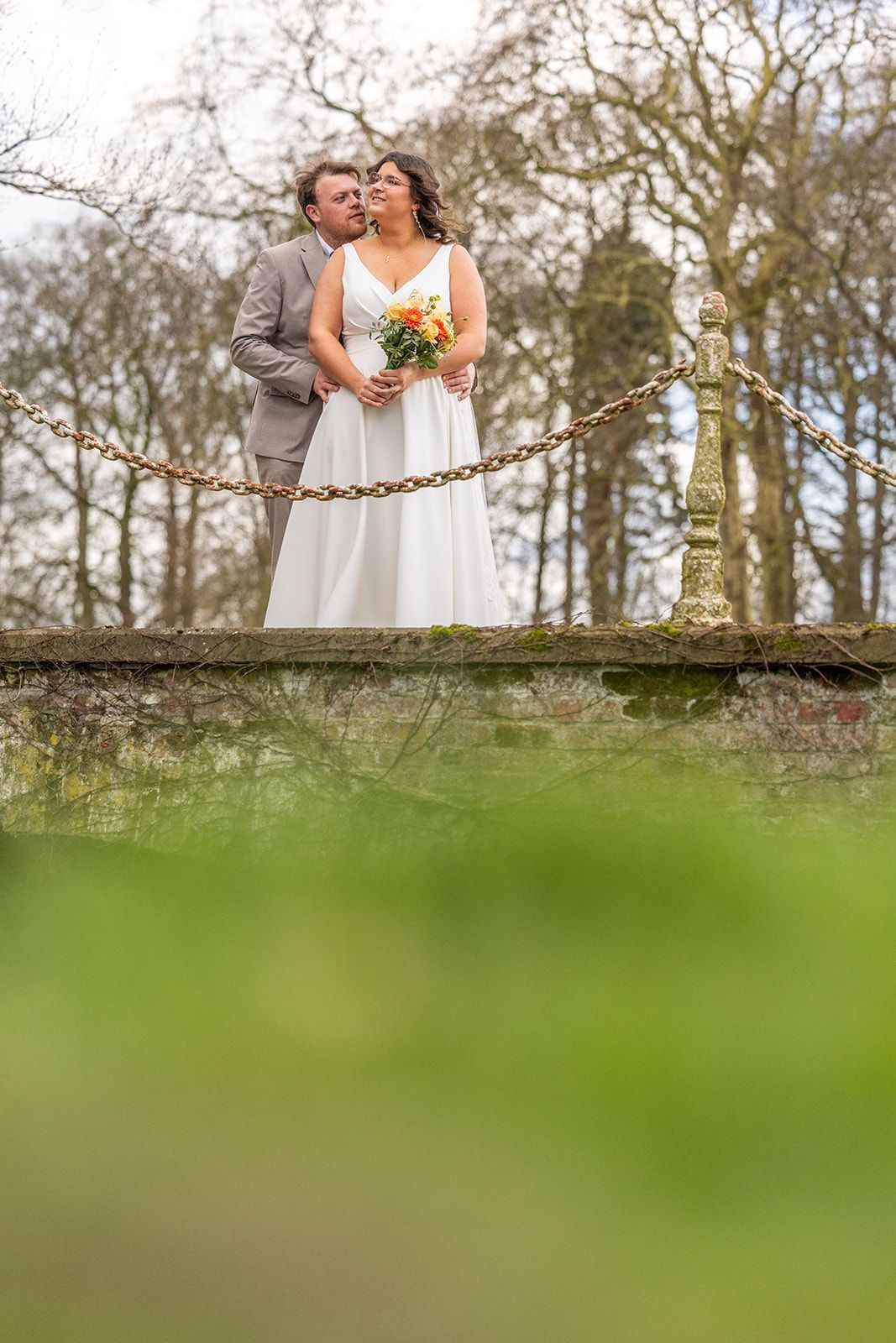 De handen van het echtpaar gevouwen, de trouwringen zichtbaar. Eén hand heeft rode nagellak, de andere draagt ​​een blauw pak.