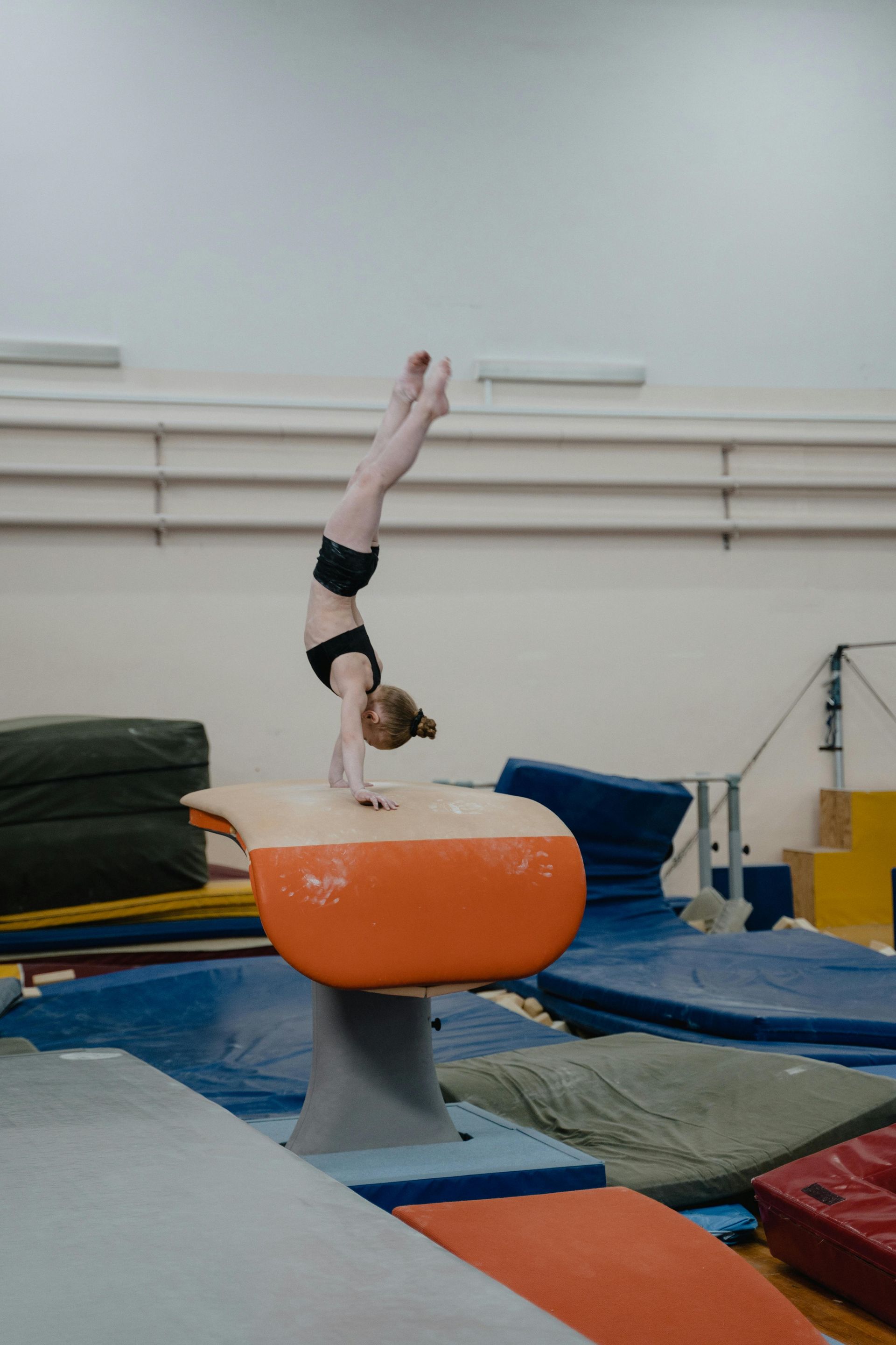 Gymnast in handstand on orange vault in a gymnasium.