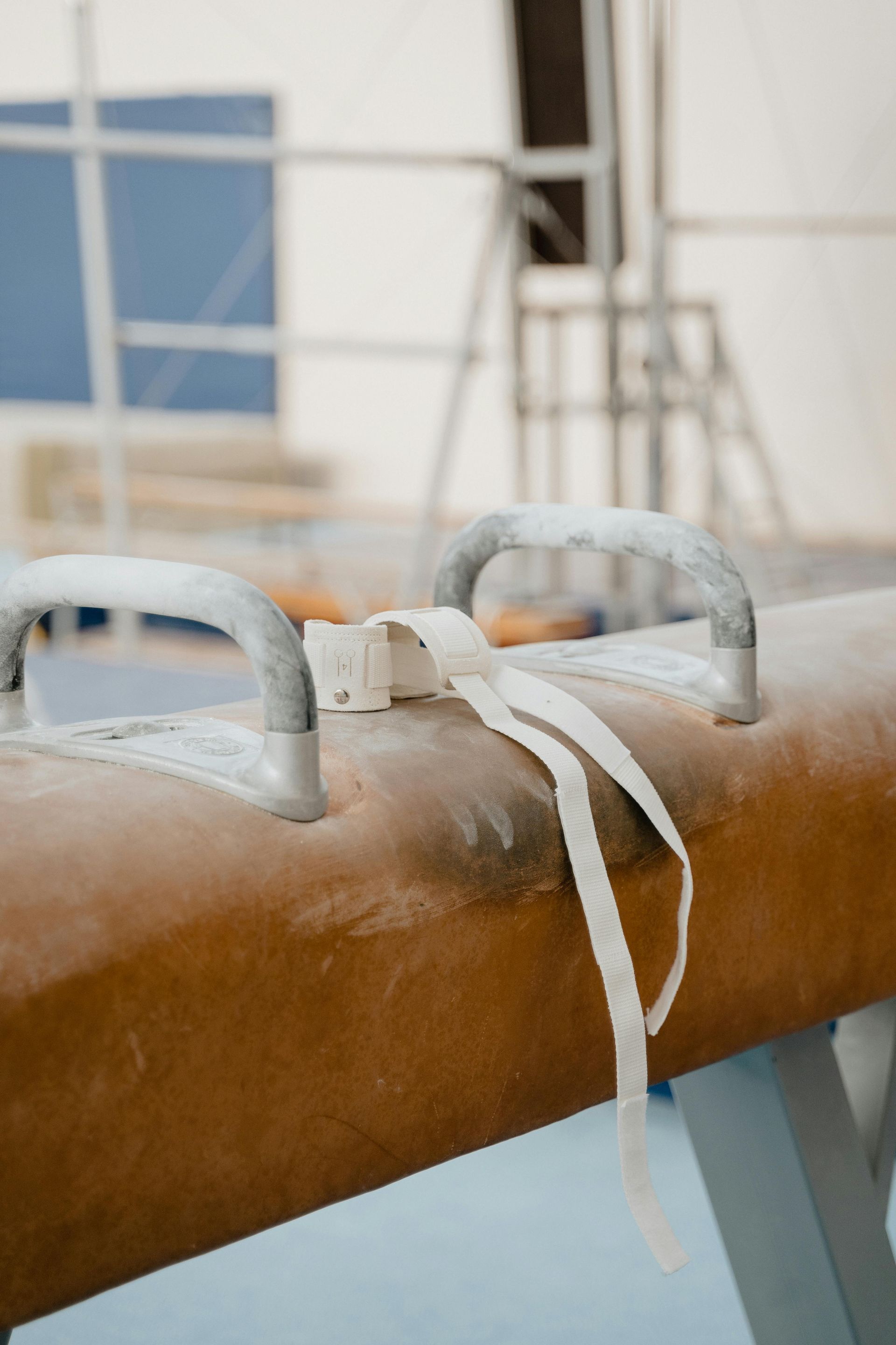 Pommel horse in a gymnasium, coated with chalk and a white strap.