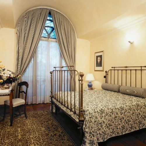 Camera da letto con letto di ottone ,tende beige e mobili di legno vecchi