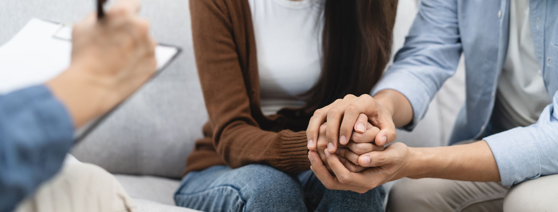 A man and a woman are holding hands while sitting on a couch.