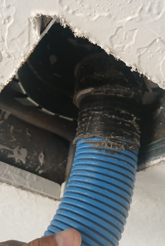 A technician in a blue uniform installs metal ductwork in an attic with foil-lined insulation.