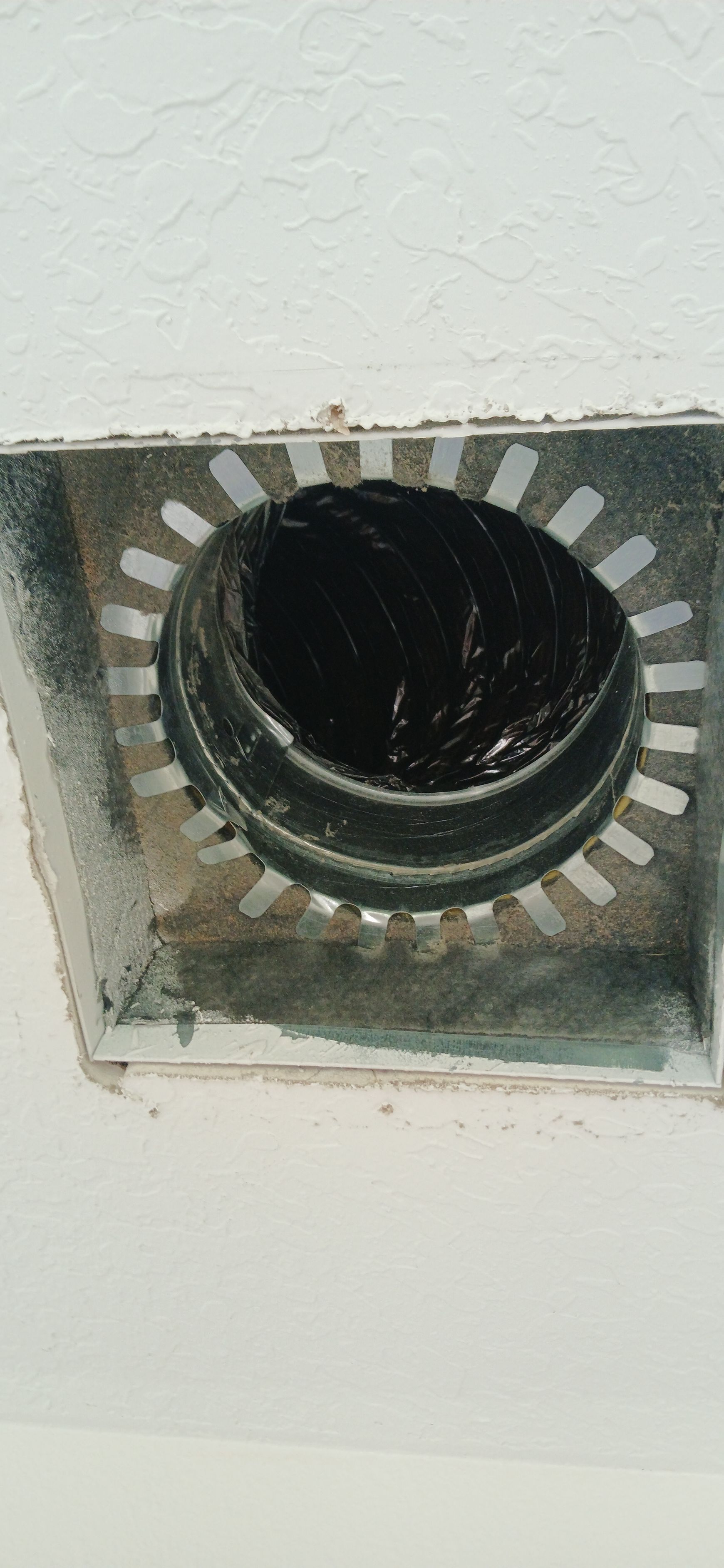 A close-up view of an open, square ceiling HVAC vent housing with a circular black duct opening centered inside.
