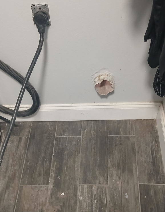 A person wearing ear protection and gloves secures a wire mesh screen over a vent opening on the exterior of a building.