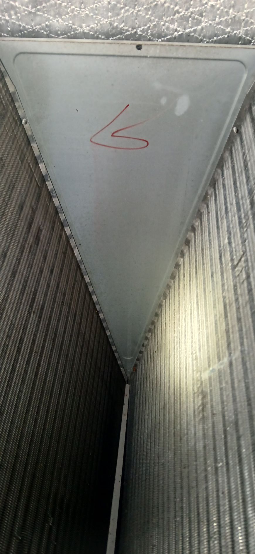 An interior view of an A-shaped HVAC evaporator coil with a metallic triangular top panel marked with a red handwritten 'L'.