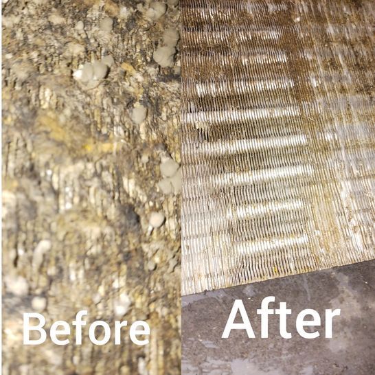 A worker in a blue shirt and dark overalls installs an outdoor air conditioning unit mounted on a white exterior wall.