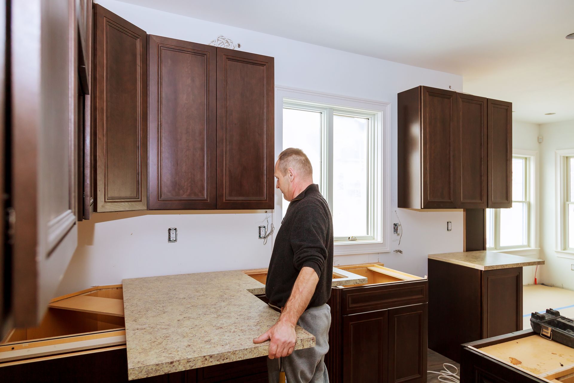 A man is installing a granite counter top in a kitchen.