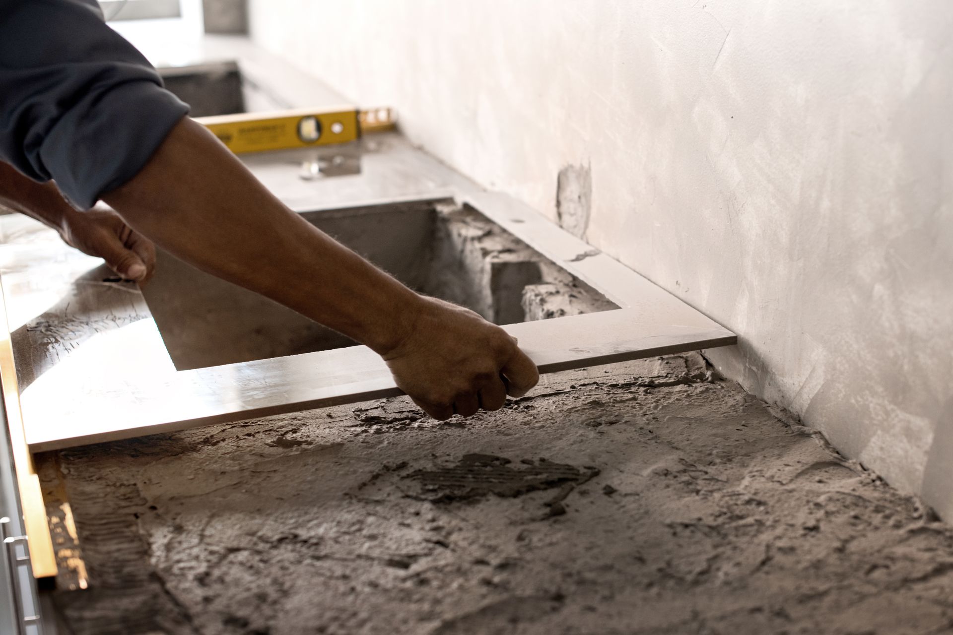 A man is laying tiles on a kitchen counter.