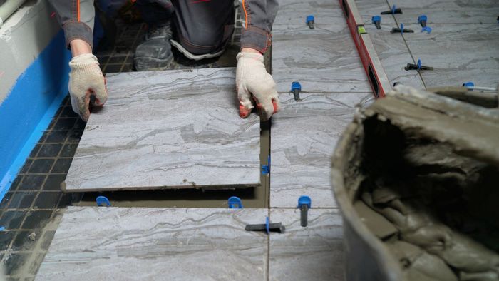 A man is laying tiles on a bathroom floor.