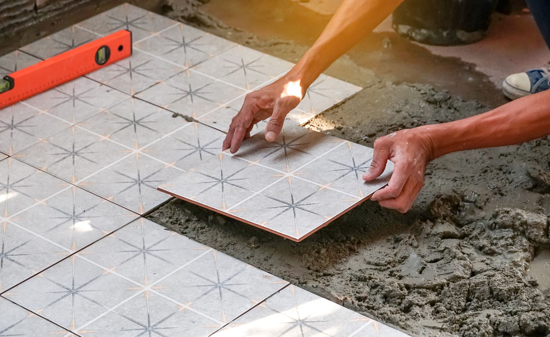 A man is laying tiles on the floor with a level in the background.
