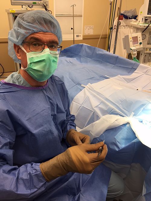 a surgeon wearing a mask and gloves is holding a needle in an operating room