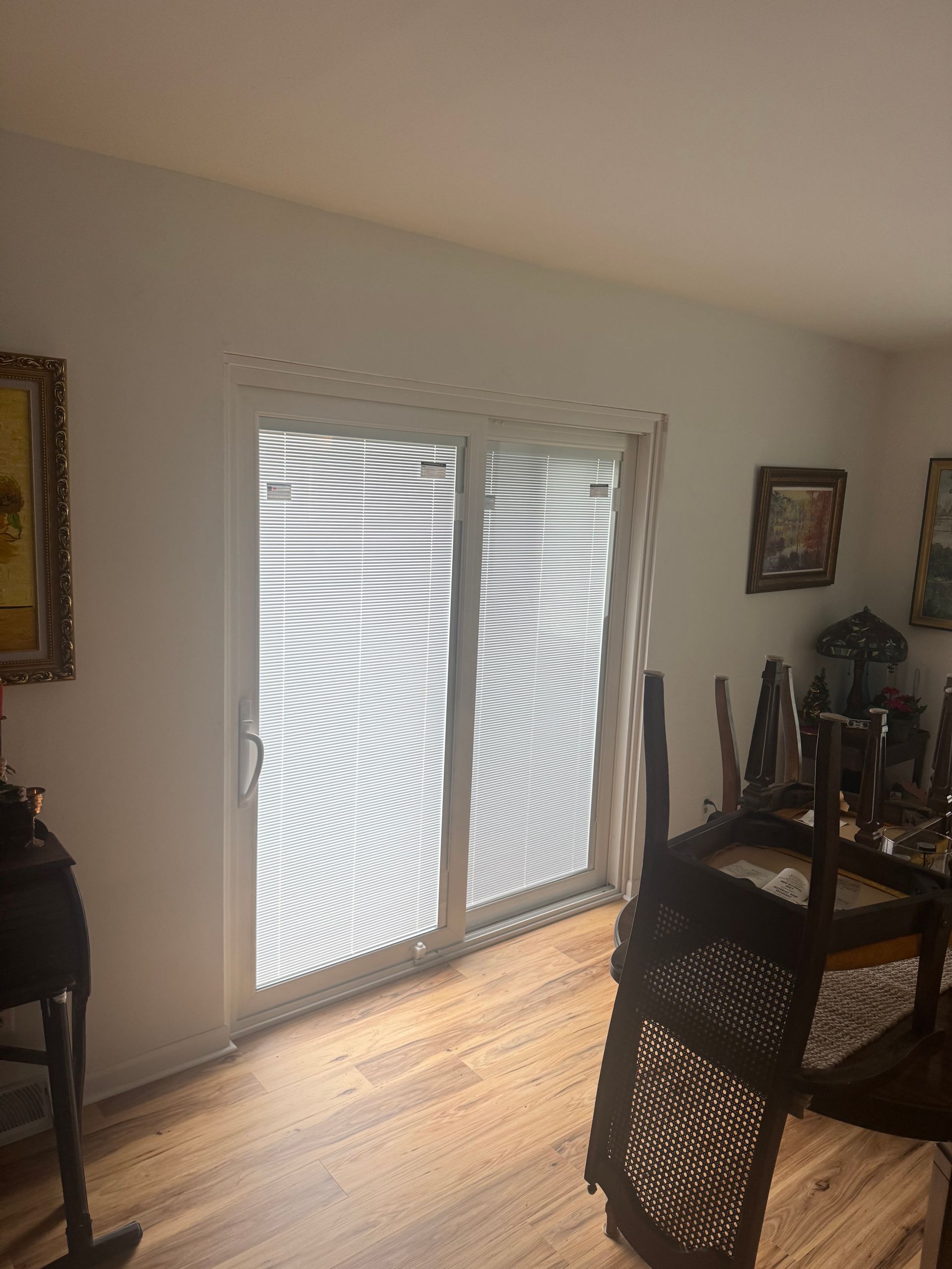 Sliding glass door with blinds, white trim, wooden floor, and dining room table in front of it.