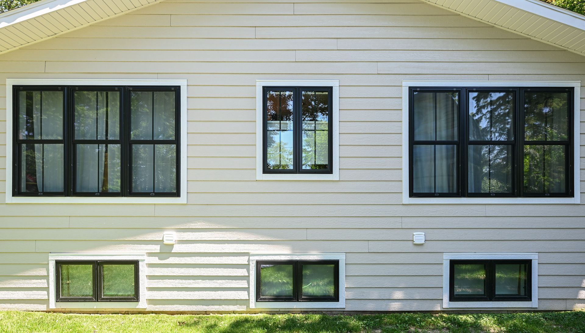Tan house exterior with black-framed windows. Three large, three small windows. Green grass in front.