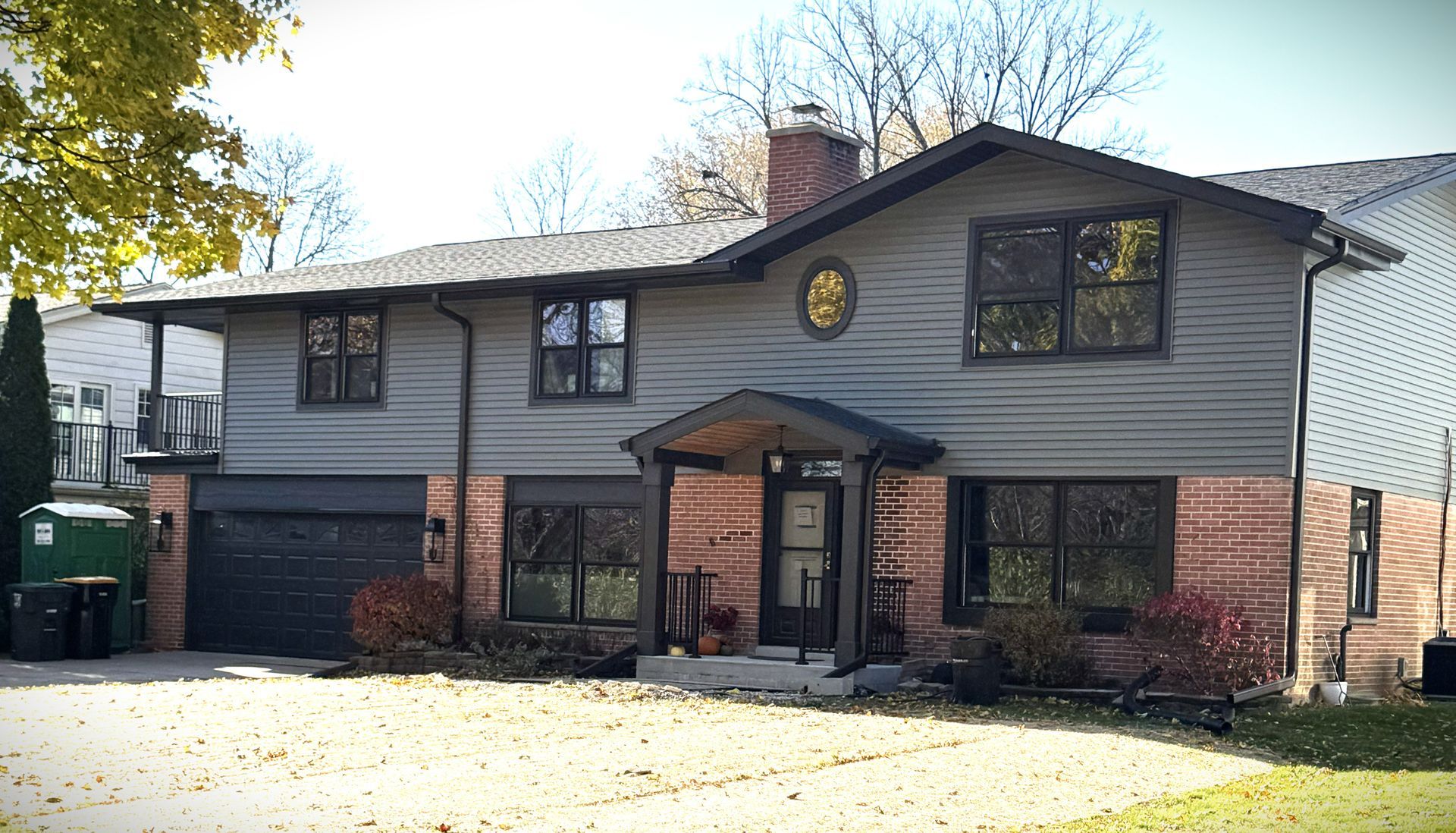 Two-story gray house with brick facade, black trim, and a small porch.