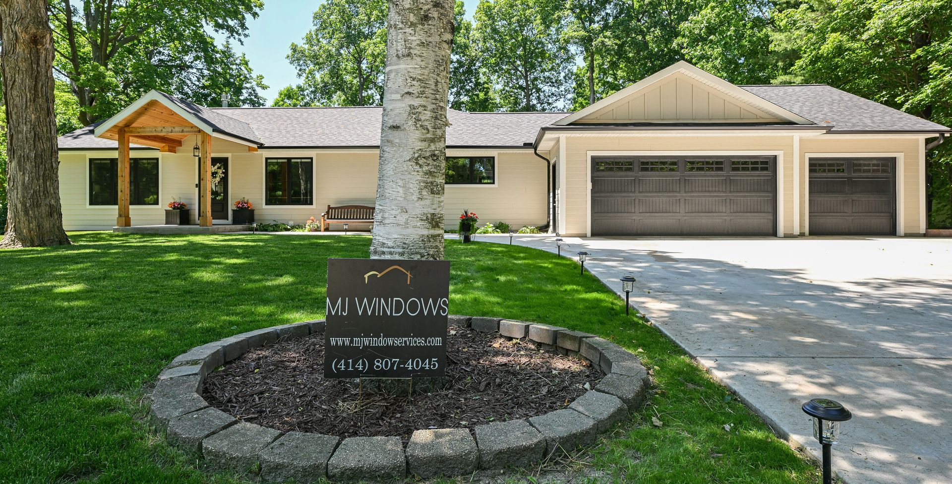 Beige ranch home with attached garage, trees, and sign in yard.
