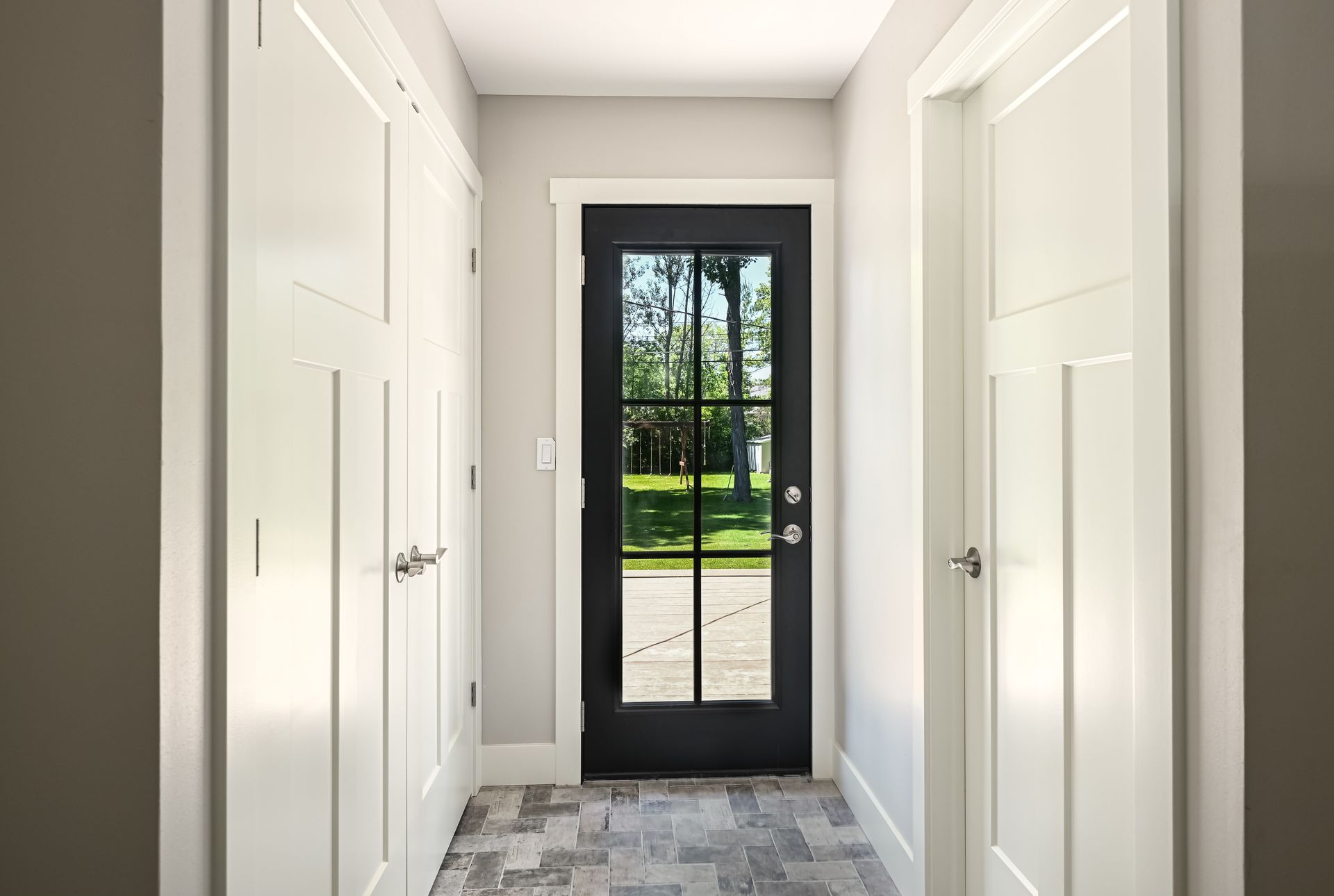 Narrow hallway with white doors, gray walls, and black-framed glass door to the outside.