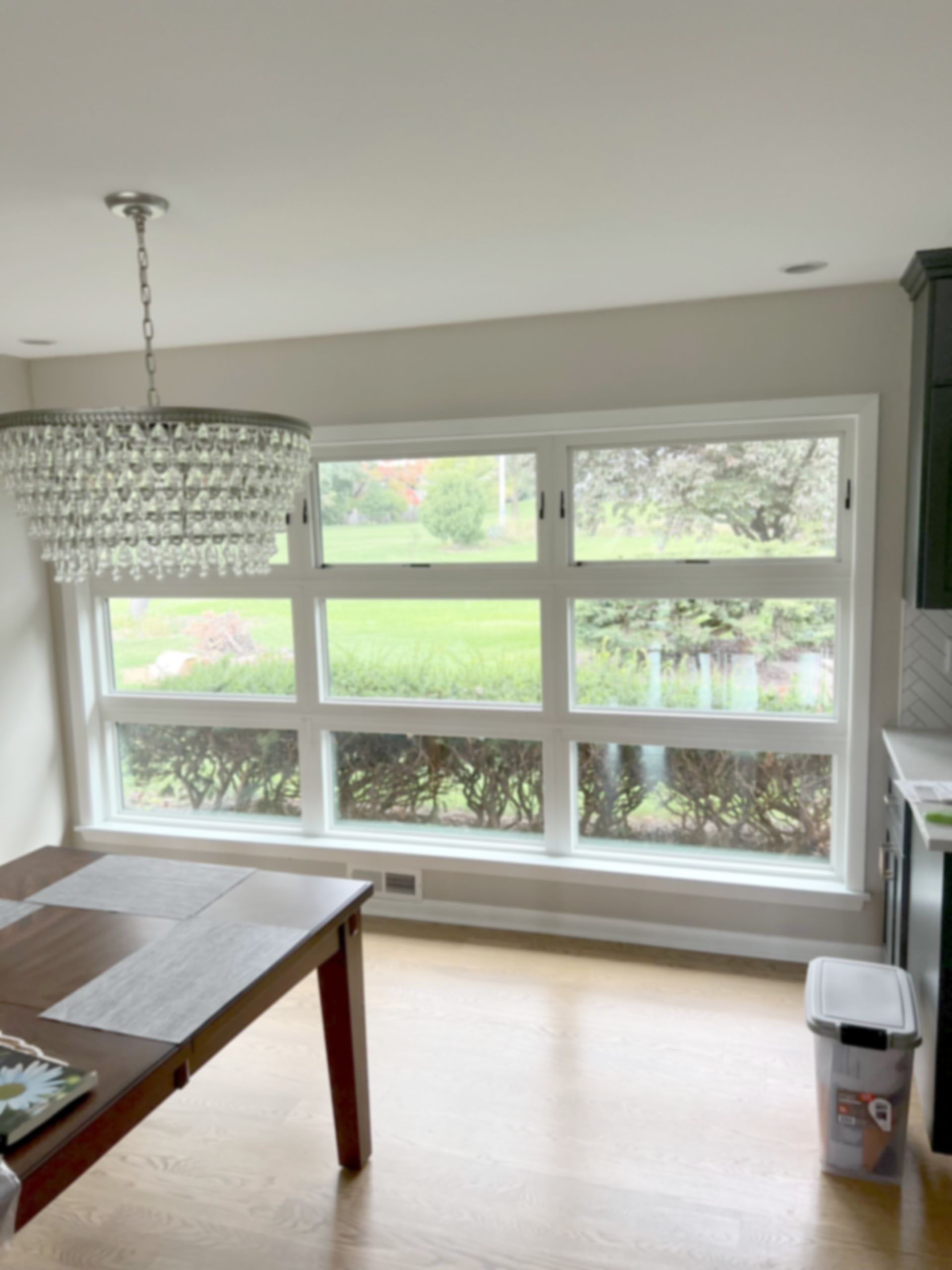 Dining area with large windows, chandelier, wooden table, and natural light.