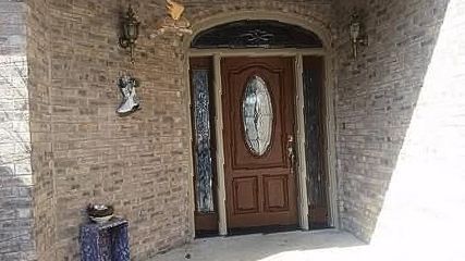 Brown door with oval window, side panels, and arched top. Set in a brick entryway.