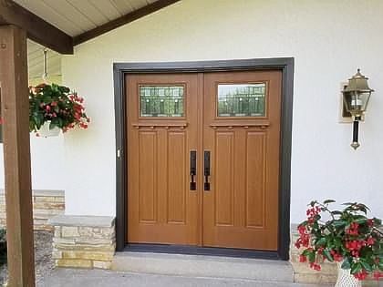 Brown double doors with glass panels and black handles; white exterior, potted flowers.
