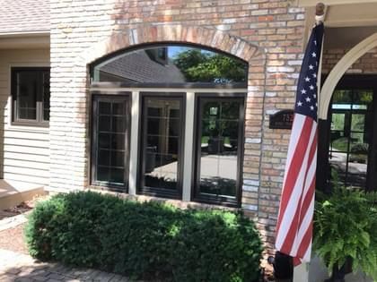Brick building facade with arched window, American flag, and bushes.
