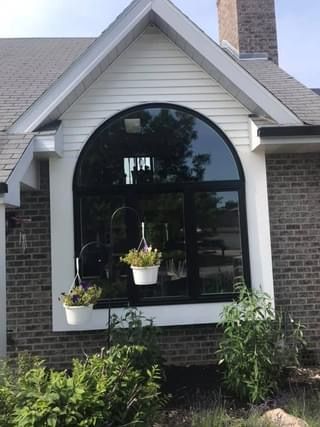 Arched window with black frame, white trim, and two hanging flower pots on a brick house.