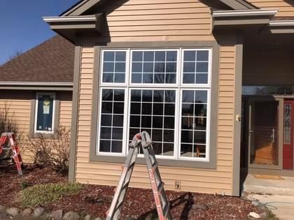 Tan house with a large grid window and white trim; a ladder leans against the window.