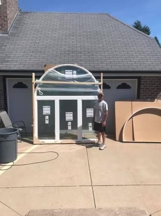 Man standing near a large, new window unit, likely for a house, on a driveway.
