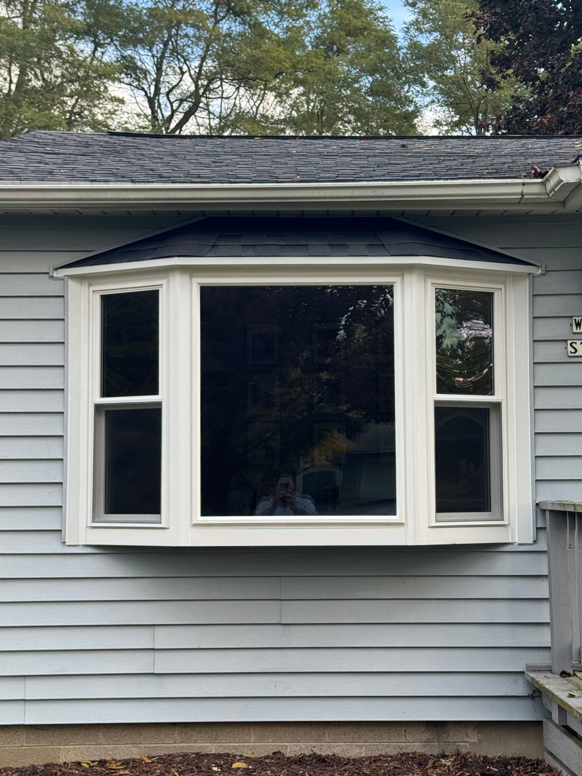 Bay window on a light blue house with a black roof, white trim.