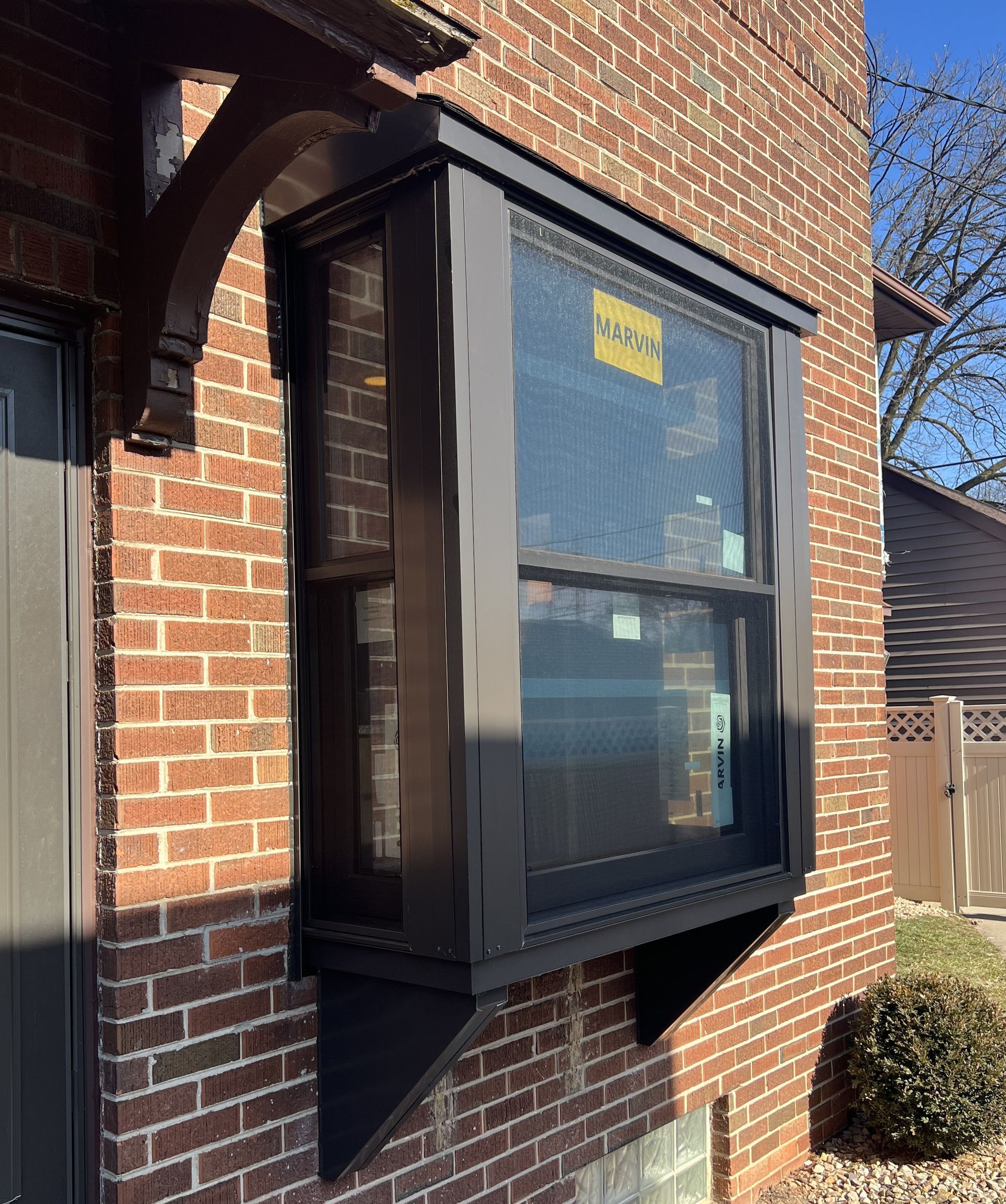 Dark-framed bay window on brick building. Angled support below, decorative bracket above.