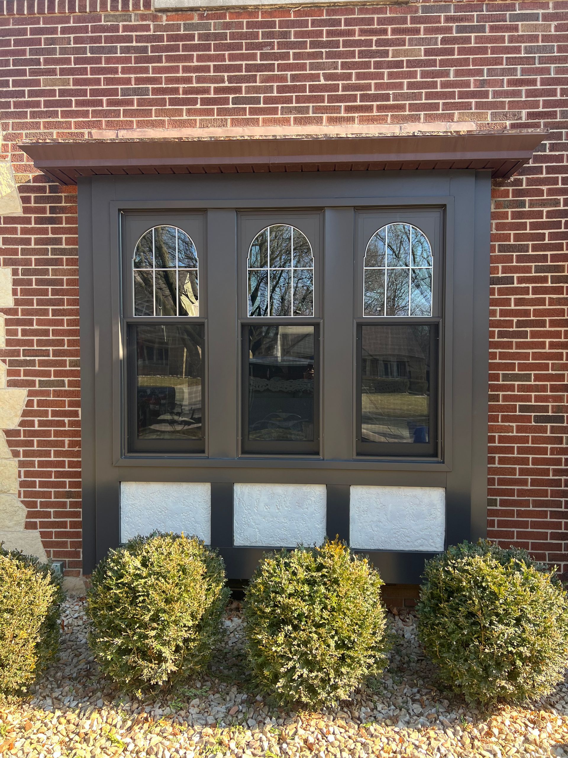A three-panel window in a dark frame on a brick building with three rectangular stone panels below the window.