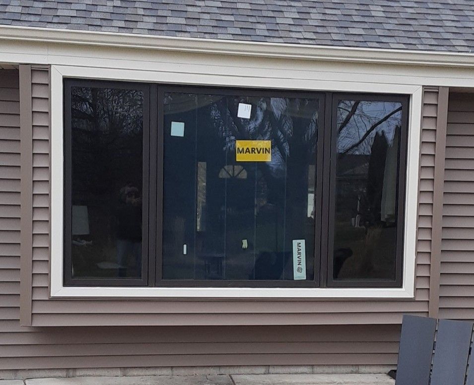 Bay window with dark frames, white trim, on a brown-sided house.