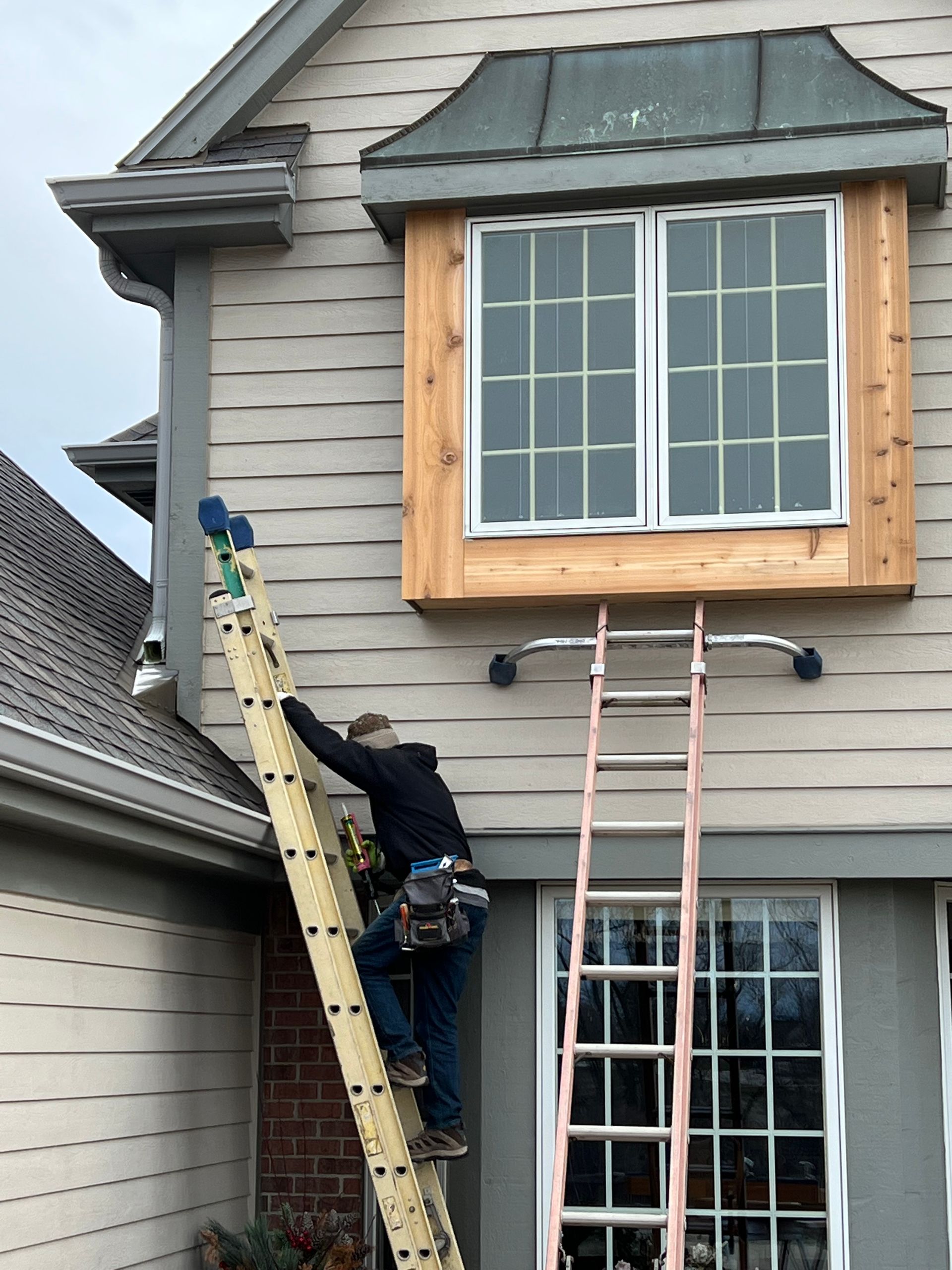 Person on a tall ladder working on the exterior of a house near a window.