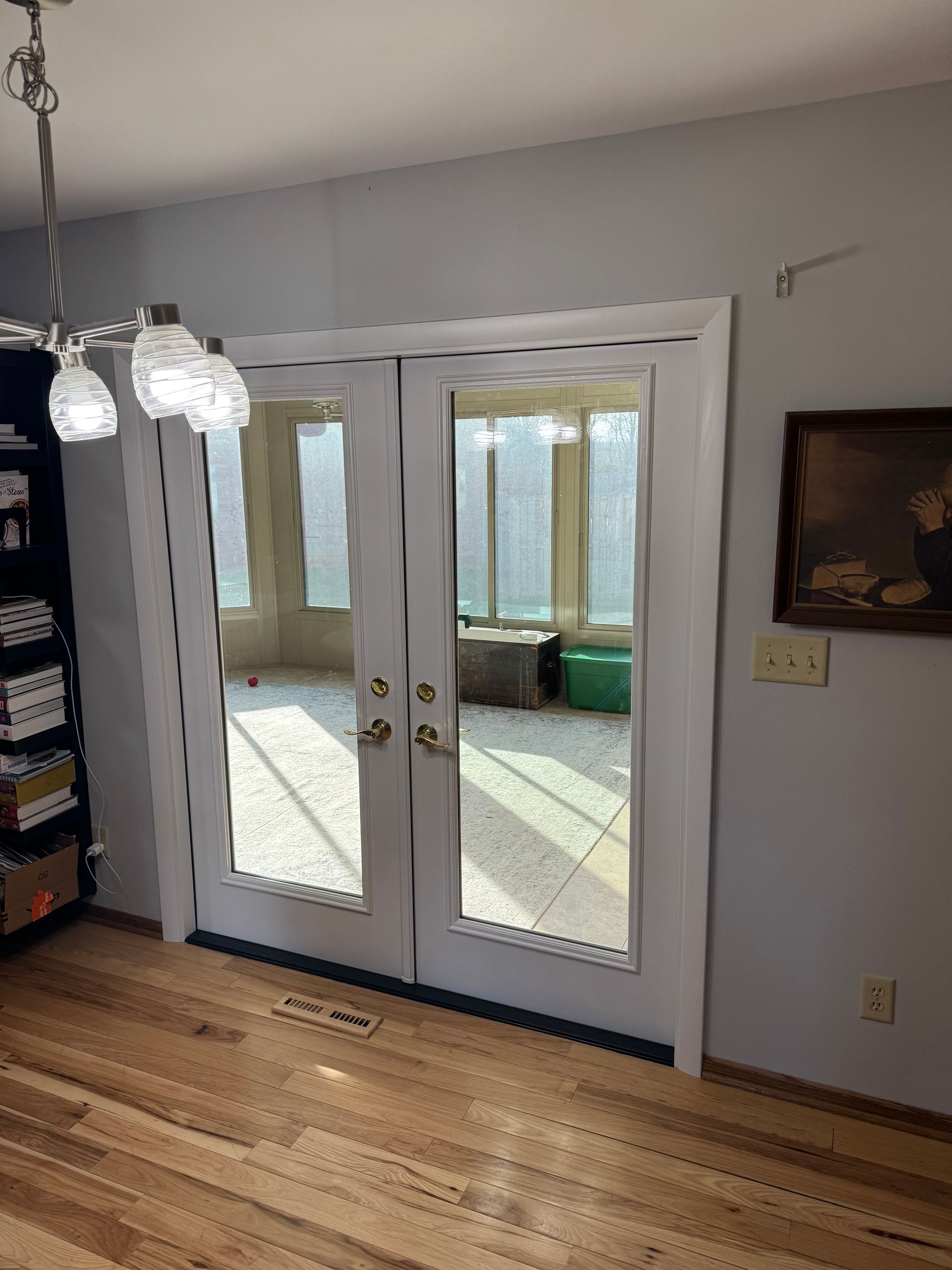 Double glass doors leading to a sunroom. White frames, wooden floor, and a hanging light fixture.