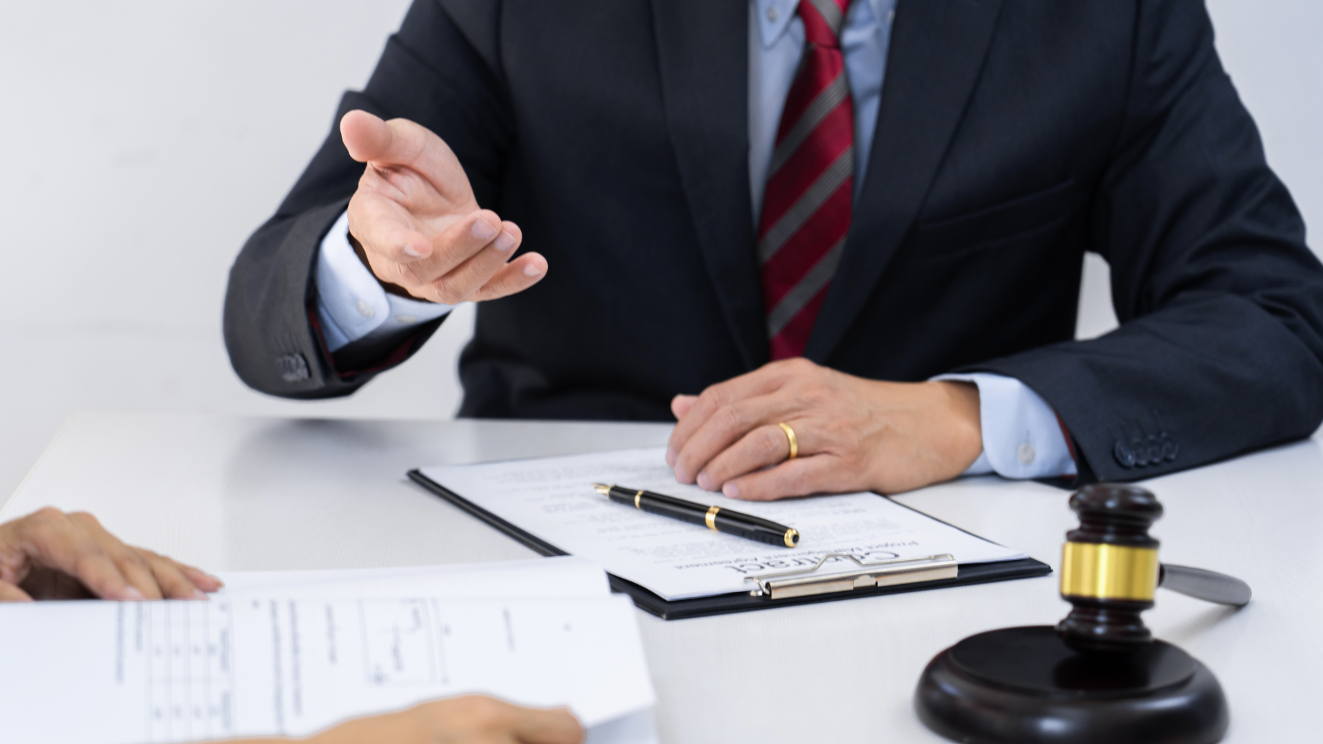 A man in a suit and tie is sitting at a table talking to another man.