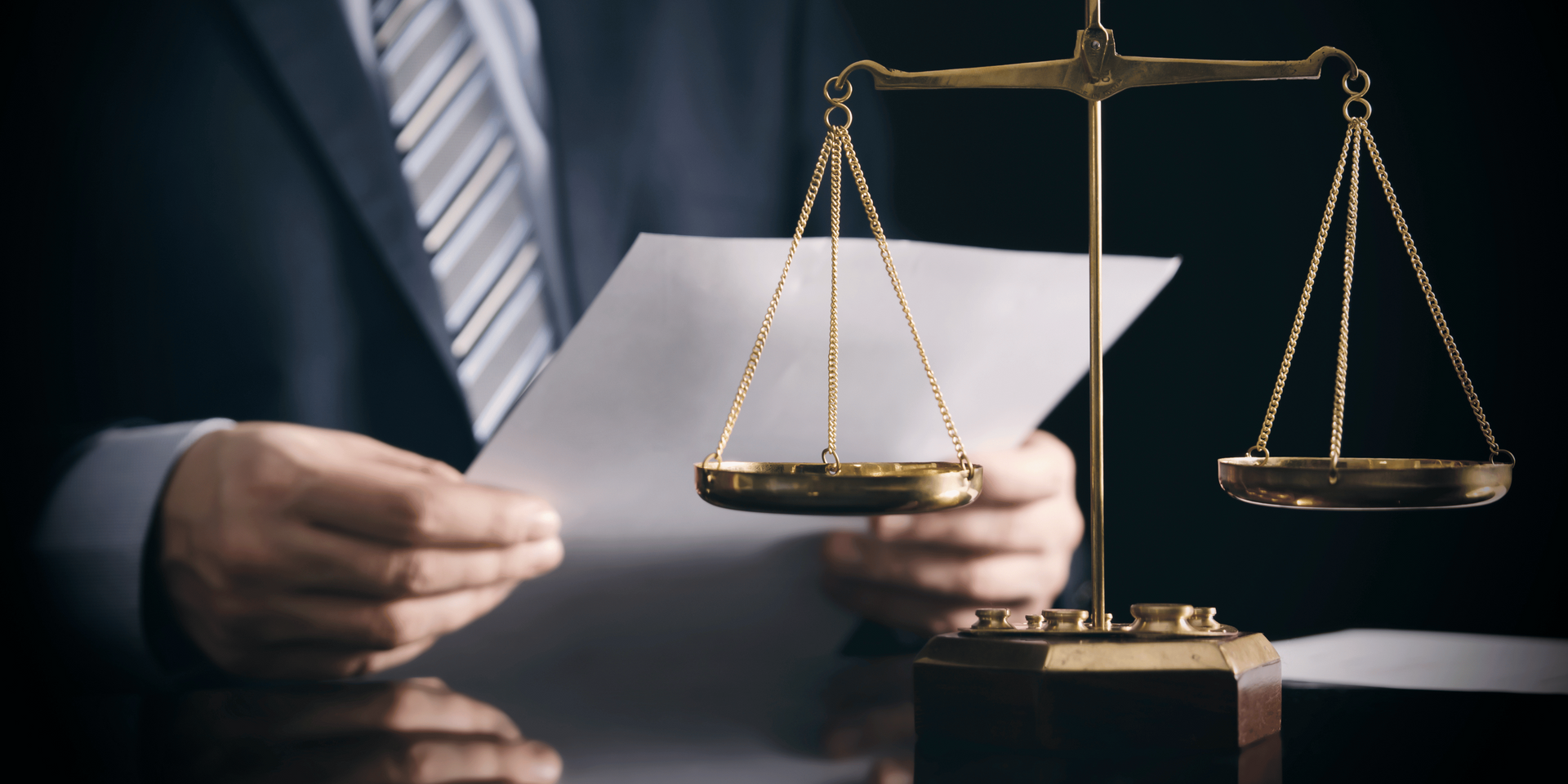 A man in a suit and tie is holding a piece of paper in front of a scale of justice.