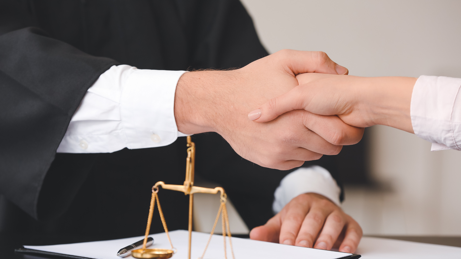 A judge is shaking hands with a client in front of a scale of justice.