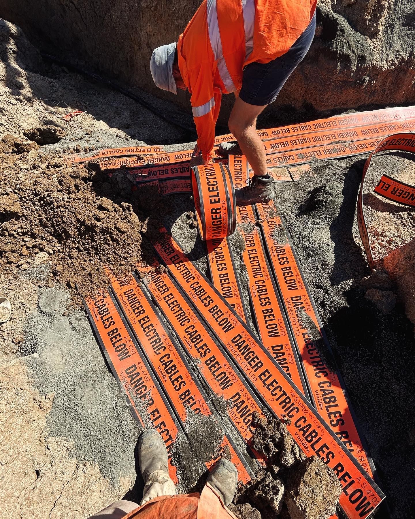 Person in Orange Vest Places Orange Danger Electric Cables Below Markers — Central West Power Construction in Orange, NSW