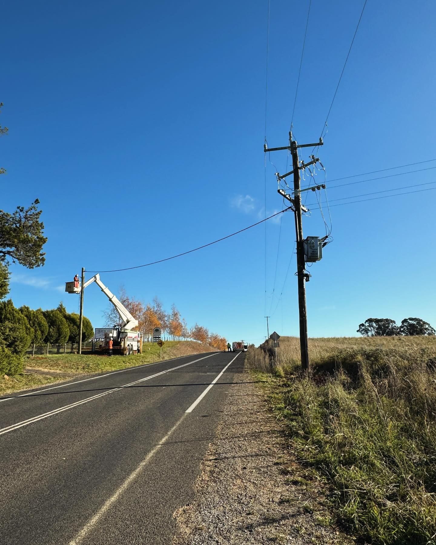 Workers in a Lift Bucket Repair Power Lines on a Road Under a Clear Blue Sky — Central West Power Construction in Orange, NSW