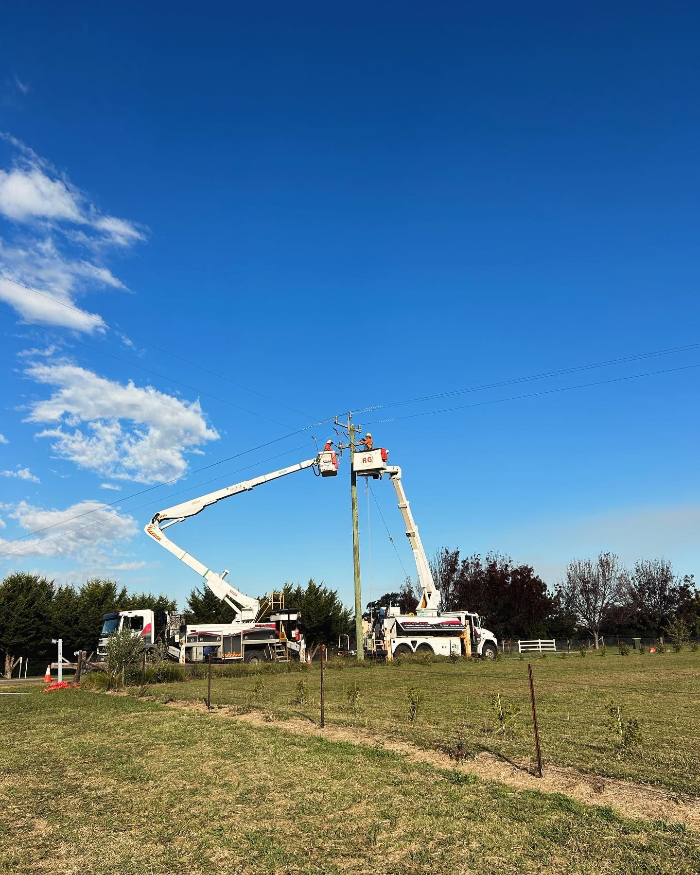 Two Utility Trucks With Raised Booms Working on a Power Pole — Central West Power Construction in Orange, NSW