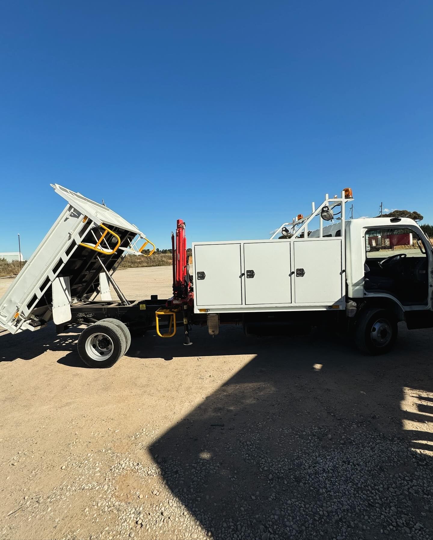 White Dump Truck With a Raised Bed, Parked on Dirt Under a Clear Blue Sky — Central West Power Construction in Orange, NSW