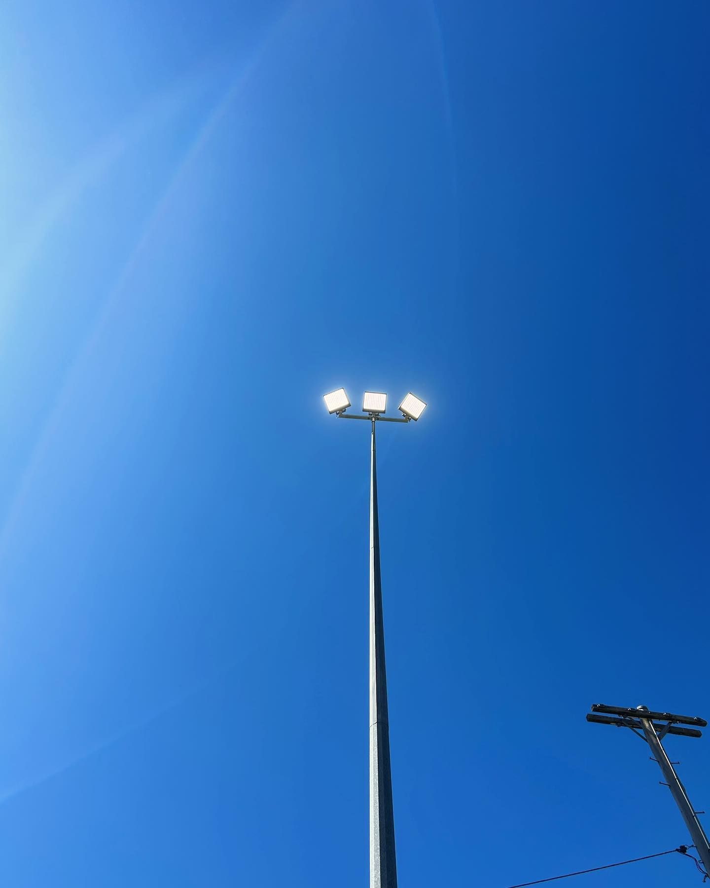 Bright Blue Sky With a Tall Light Pole Holding Three Bright Lights — Central West Power Construction in Orange, NSW