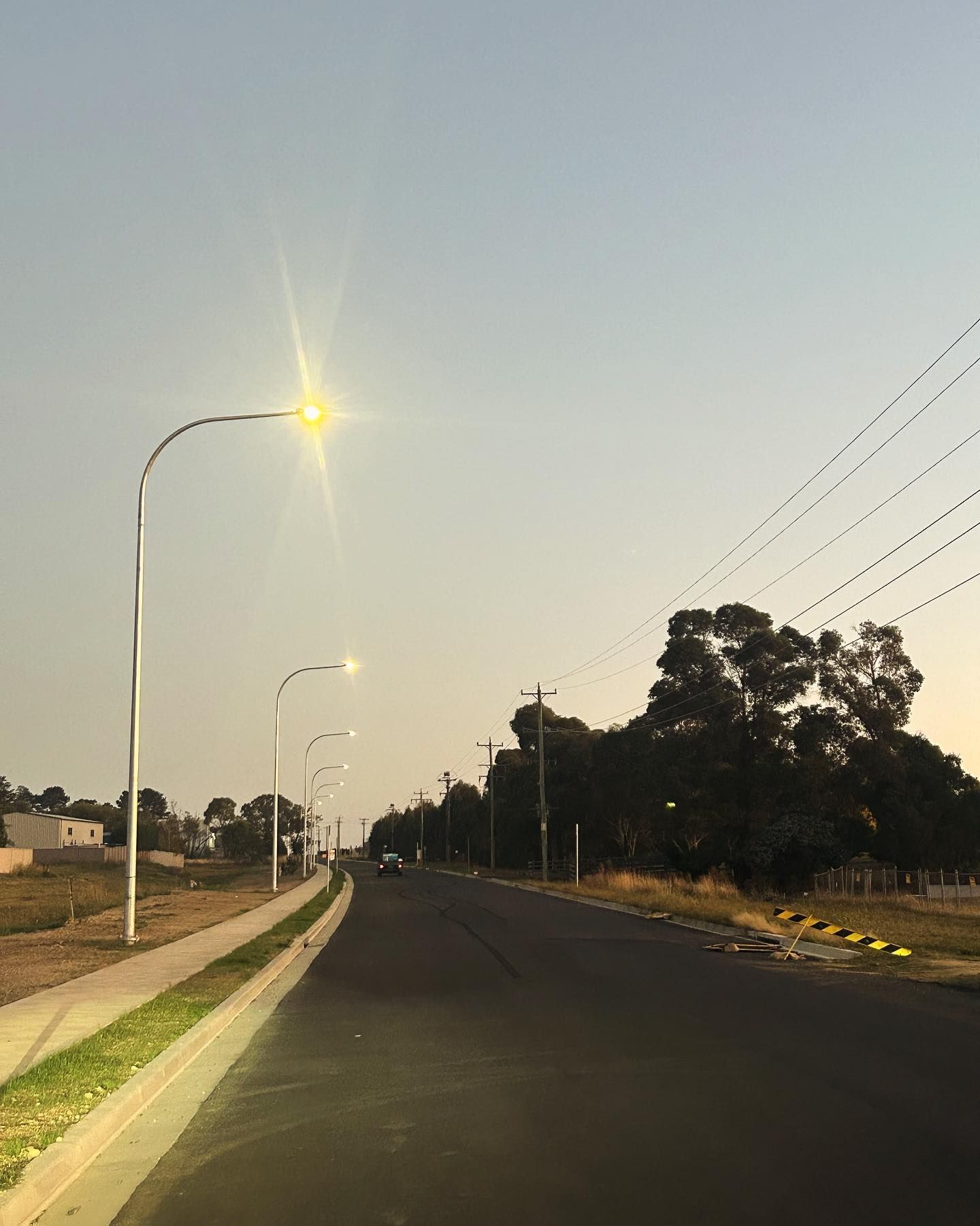 Street Scene With Lampposts Lit, Asphalt Road, and Trees Under a Pale Sky — Central West Power Construction in Orange, NSW