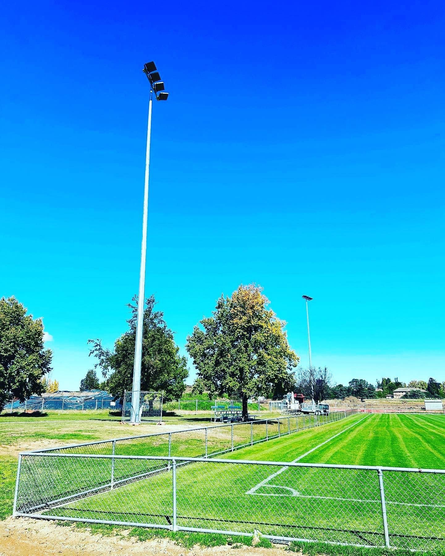 Soccer Field With Tall Lights, Green Grass, Trees, and a Blue Sky — Central West Power Construction in Orange, NSW
