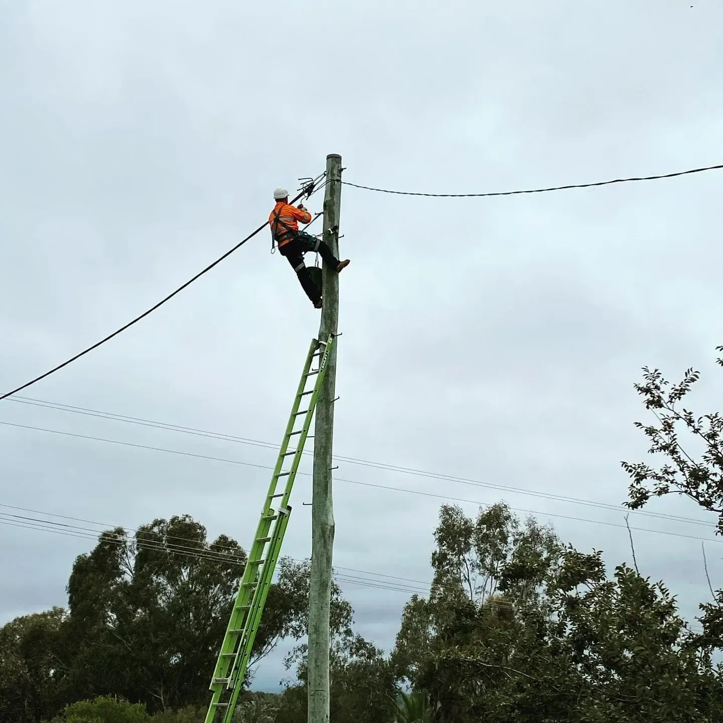 Lineman on Utility Pole With Ladder, Working on Electrical Lines, Cloudy Sky — Central West Power Construction in Orange, NSW